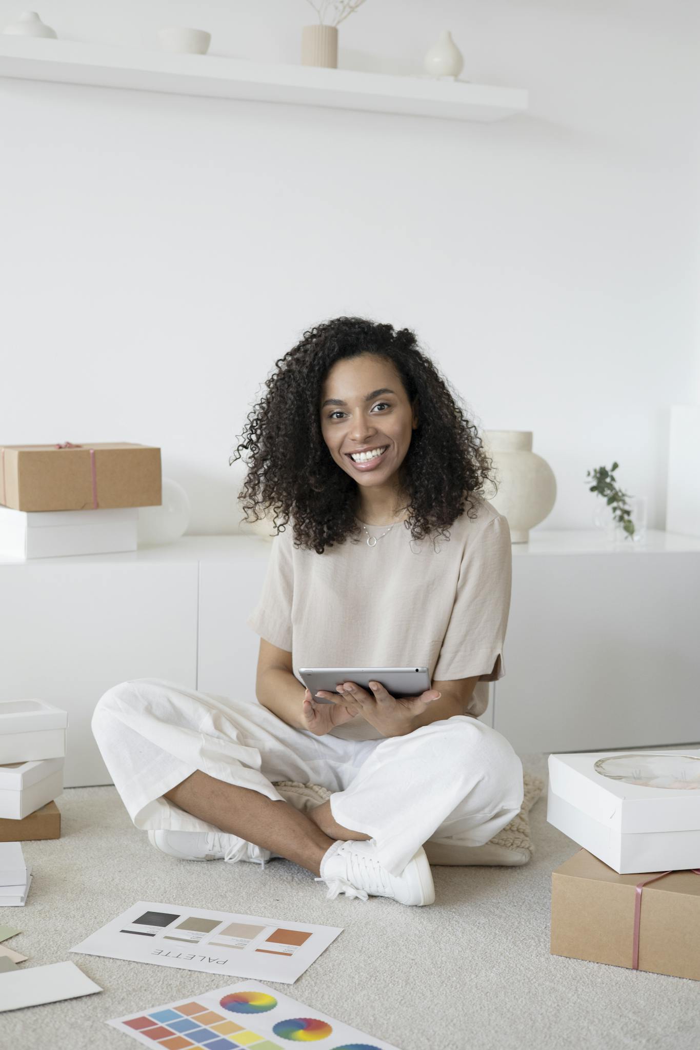 A confident young woman sitting among packages and papers while using a tablet, showcasing modern entrepreneurship.