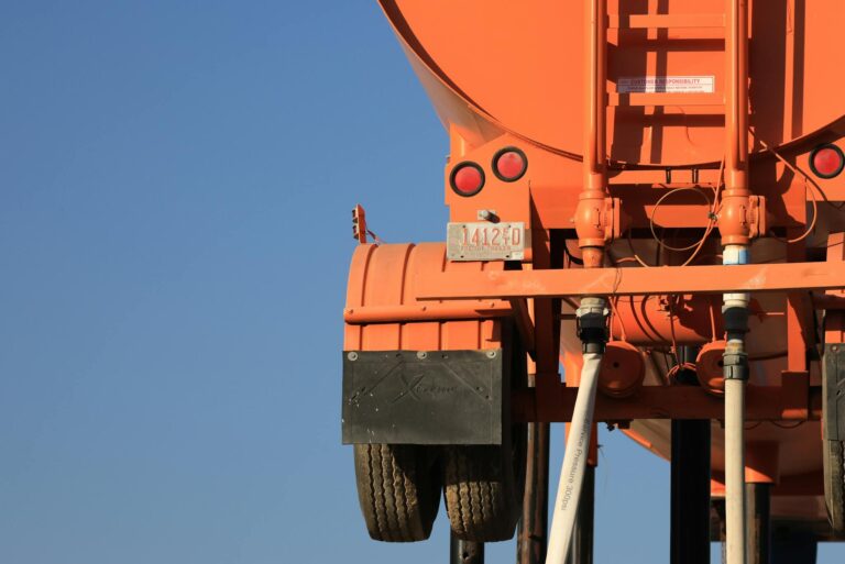 Bright orange tanker truck rear view against clear blue sky, showcasing industrial design.